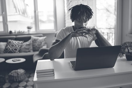 An African-American male is resting his chin on his interlaced fingers and his elbows propped on a d...