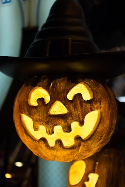 Halloween Jack o Lantern pumpkin with hat, emitting light at night. Concept of celebration, day of t...