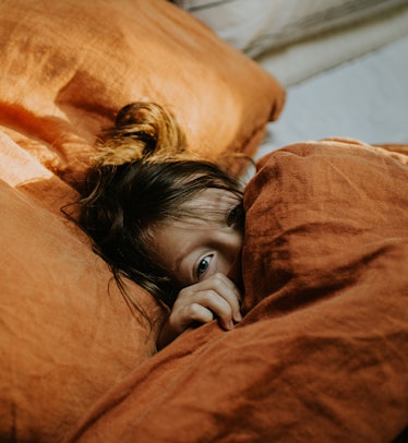 一个可爱的年轻女孩躺在一张舒适的双人床上，裹着厚厚的羽绒被与一个陶土彩色李…