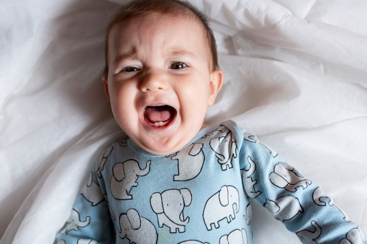 A baby in pajamas in bed crying.