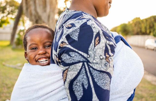 Close-up of cute boy sitting back wrap sling of his mother walking outside. The name Ethan is a stro...