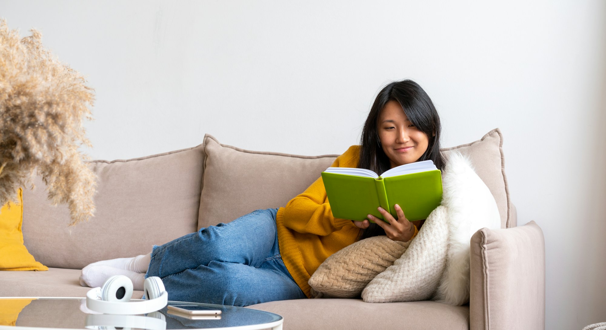 Intelligent asian female lying on couch and reading book. Taking technology break and limiting scree...