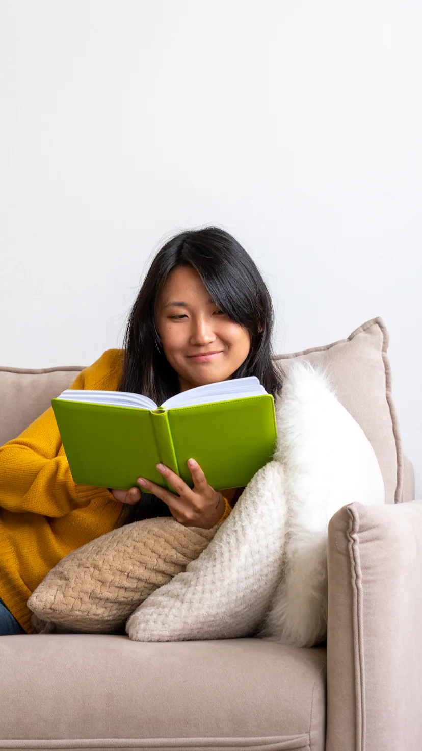 Intelligent asian female lying on couch and reading book. Taking technology break and limiting scree...