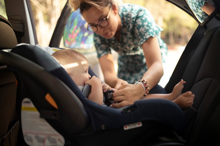 Woman puts a seat belt on her baby boy, who is sitting in a car seat.
