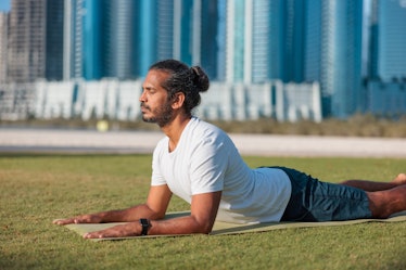 Man practicing yoga on the lawn in public park in Abu Dhabi, lying on front and leaning on elbows in...