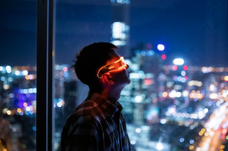A man looking through a window during night time with smart glasses with blurred city lights in the ...