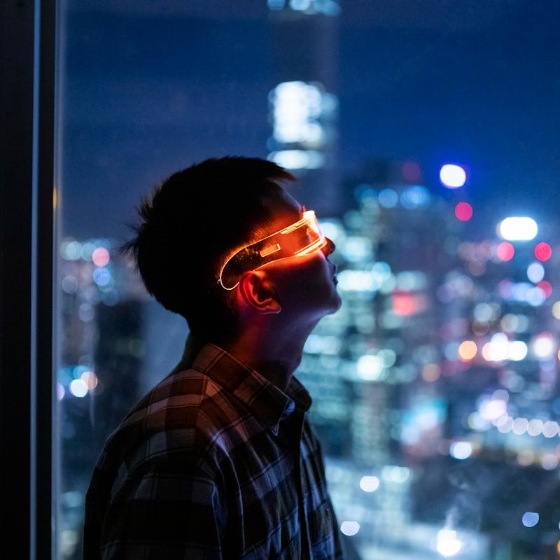 A man looking through a window during night time with smart glasses with blurred city lights in the ...