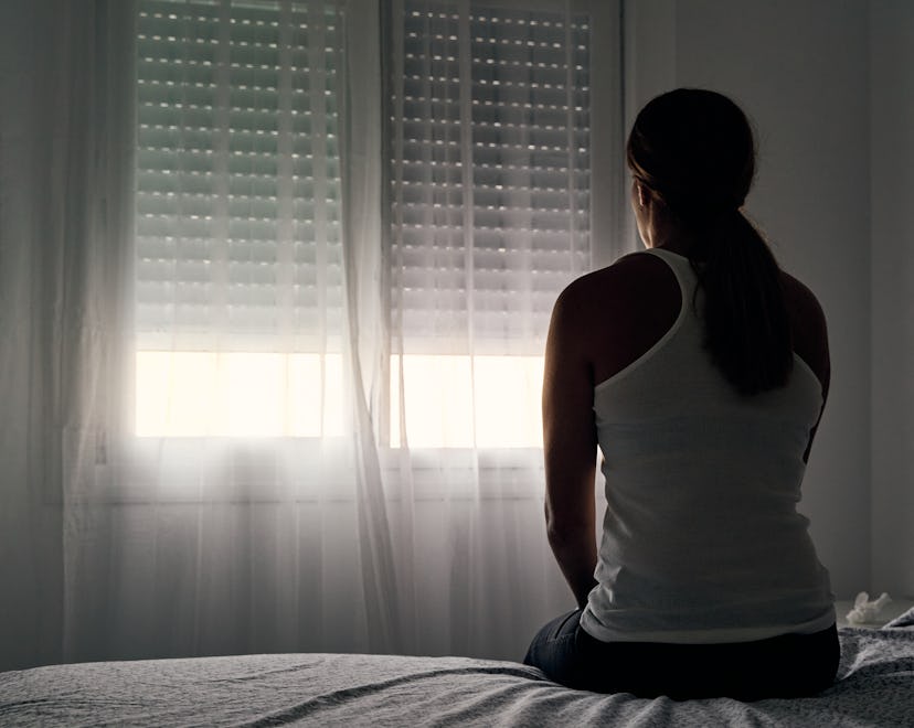 Rear view of an unrecognizable woman sitting on her bed in an article about missed miscarriage and ...