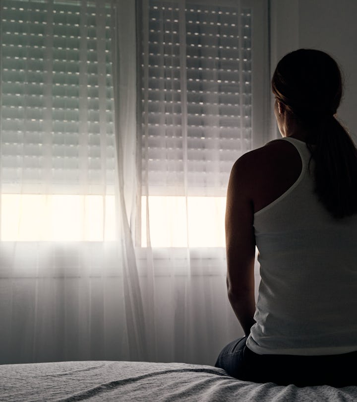 Rear view of an unrecognizable woman sitting on her bed  in an article about missed miscarriage and ...