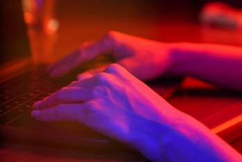 Neon light illuminated hands typing on a computer keyboard