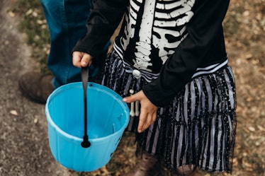 Little Australian girl in skeleton costume holds her empty blue trick or treat bucket on Halloween
