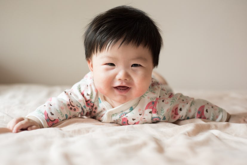 Front view of a 5 months old baby boy lying on bed and outstretching his arms in a round up of baby ...