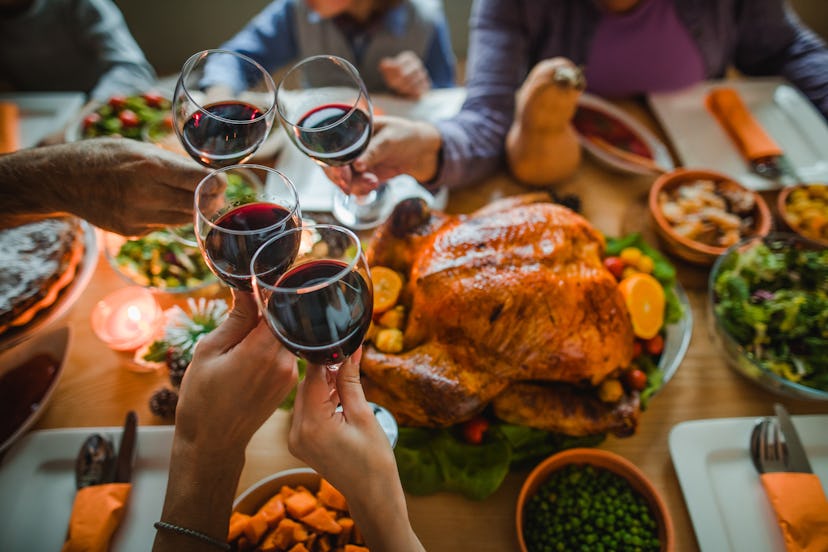 Group of unrecognizable people toasting with wine during Thanksgiving dinner at dining table. what w...