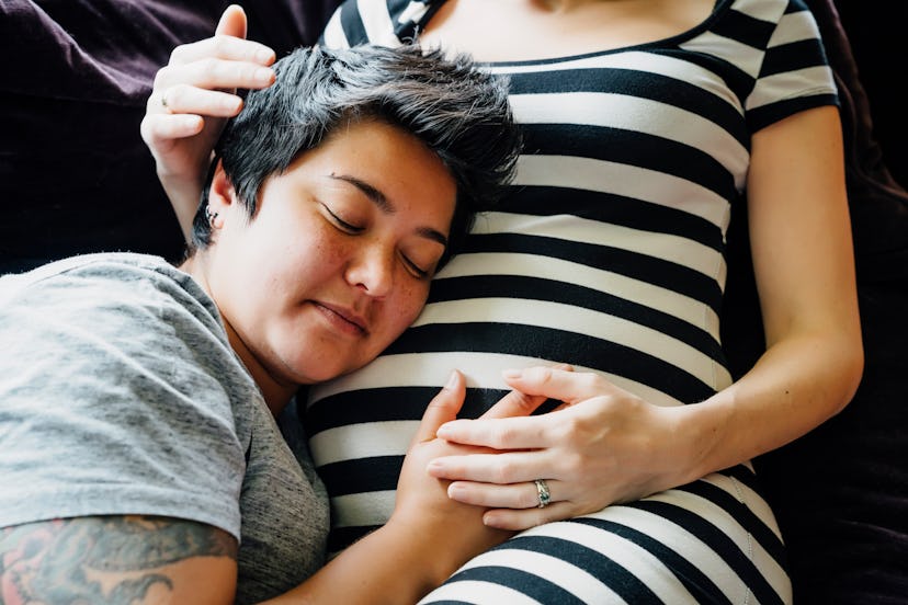 a couple expecting a baby, with one person's head resting lovingly on the other persons pregnant bel...