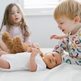 Two little kids sitting on a bed and playing with their baby sibling