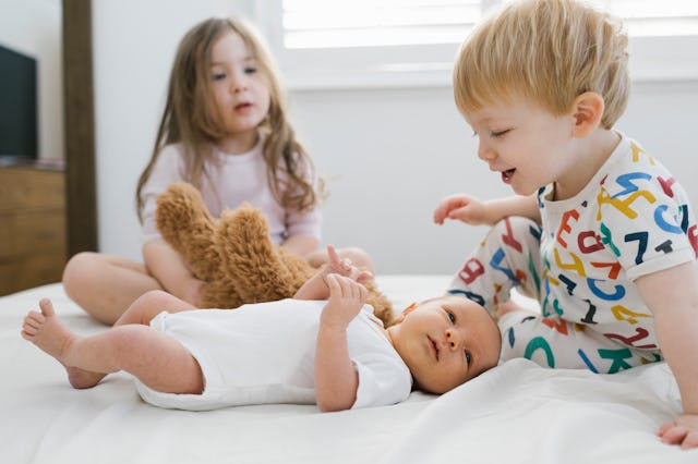 Two little kids sitting on a bed and playing with their baby sibling