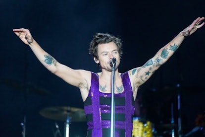 Harry Styles performs on stage with his tattoos showing.