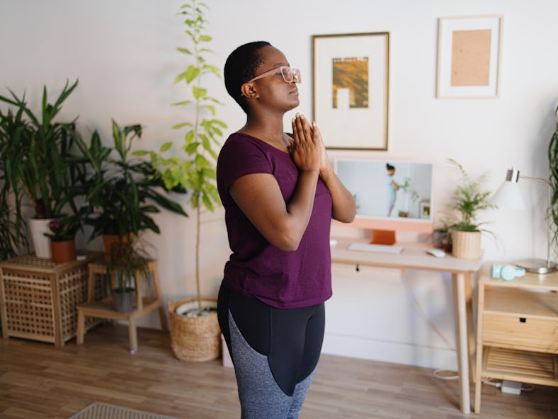 A woman begins to follow a guide to Sun Salutations in yoga at home. 