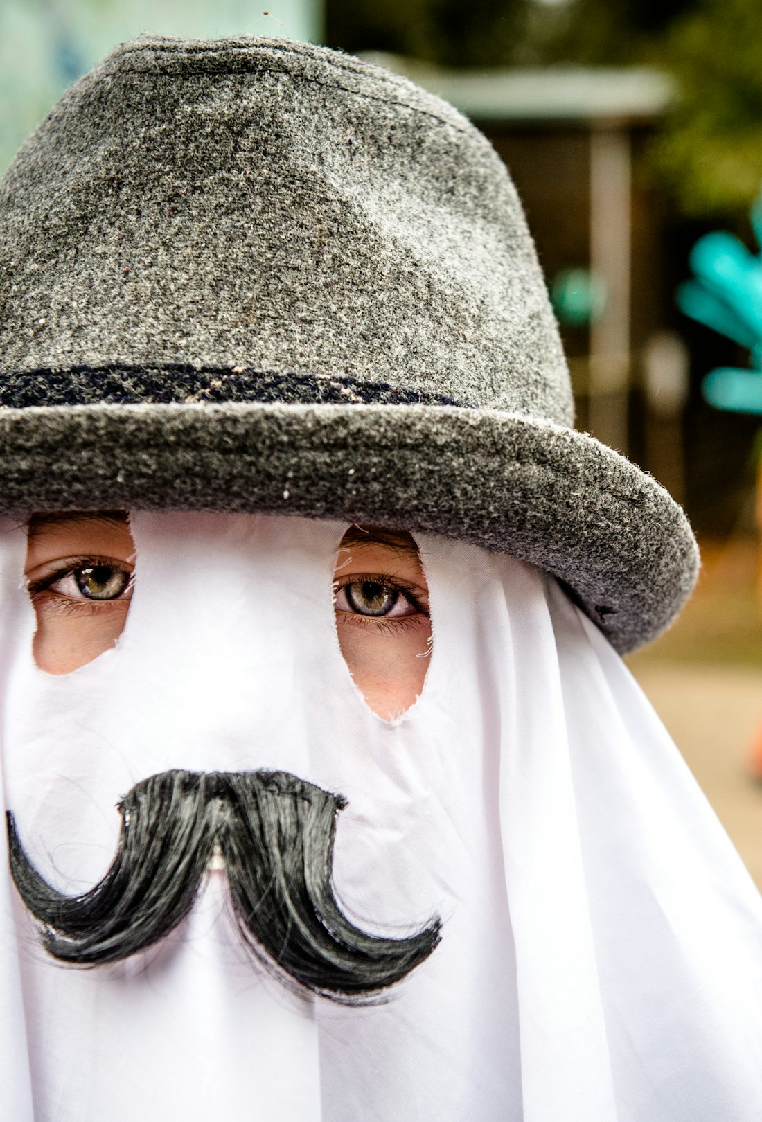 Child wearing a last-minute Halloween 2022 costume; a ghost sheet with fedora and mustache.