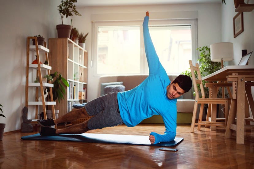 A man does a side plank at home on a yoga mat.