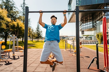 A handsome young Chinese man doing pull-ups on a bar outdoors in a public park.