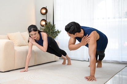 A man and woman do high plank single arm swaps at home, tapping one shoulder from a high plank posit...