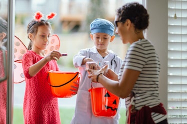 A pair of siblings trick-or-treating together around the neighborhood. A woman is giving them candy ...
