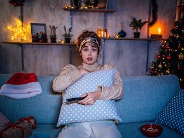 Young scared woman watching horror movie in the living room at night during Christmas holidays