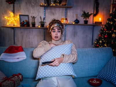 Young scared woman watching horror movie in the living room at night during Christmas holidays