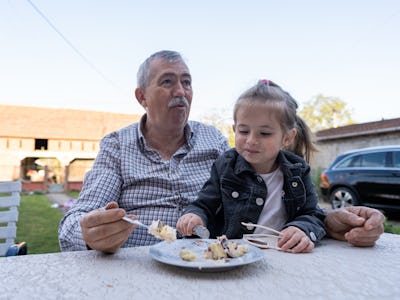 Caucasian grandfather and granddaughter together eating birthday cake