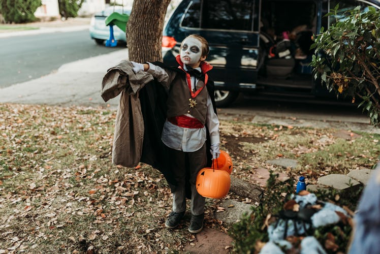 A little boy dressed as a vampire with a pillowcase in his hand is trick or treating