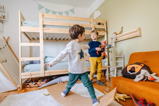 Photo of little boy playing with balance board in his room, while his brother is playing with dinosa...