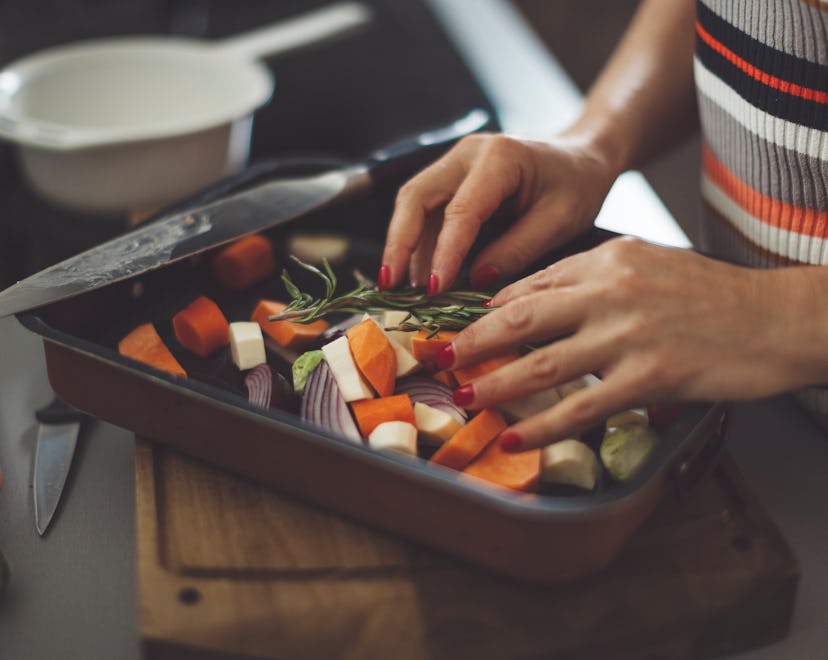 Hands arranging sweet potatoes, onions, and other vegetables on a baking sheet to prepare a sweet po...