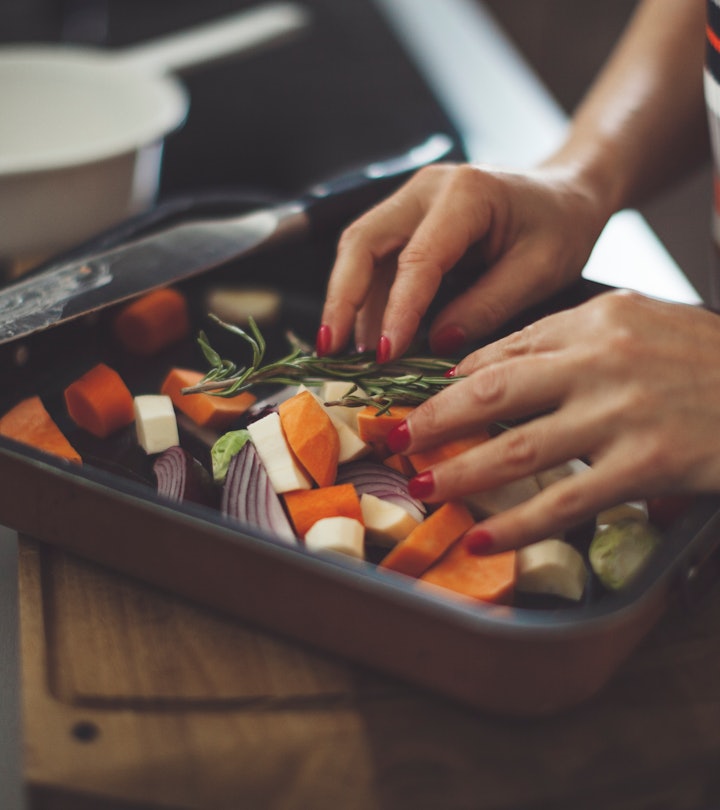 Hands arranging sweet potatoes, onions, and other vegetables on a baking sheet to prepare a sweet po...