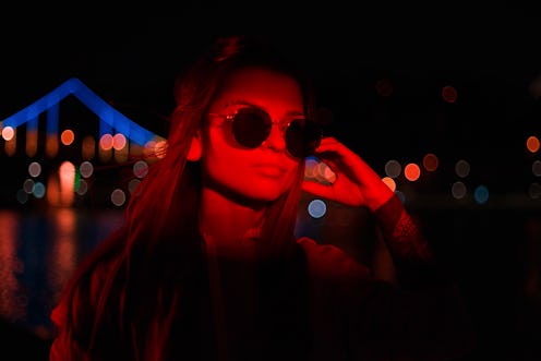 Close-Up Portrait Of Sensual Young Woman Wearing Sunglasses illuminated With Blue and Red Neon Light...