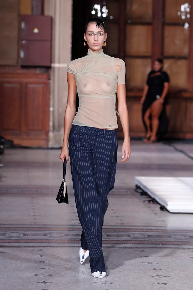 A model wearing Coperni nude transparent t-shirt and line pattern navy pants at Paris Fashion Week S...
