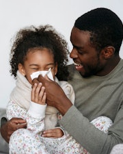 a father helps his daughter blow her nose. article about cough and cold medicines for kids.