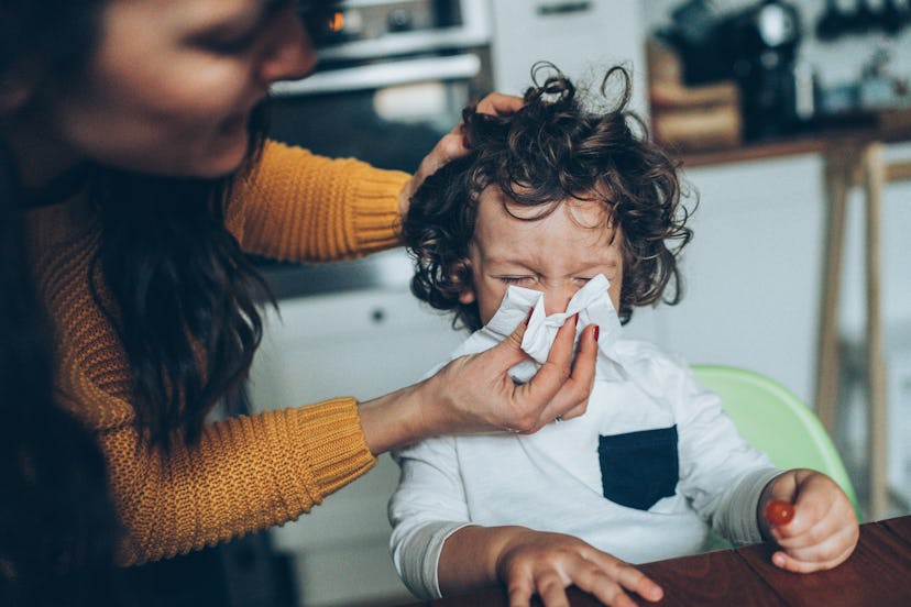 Mother helping son to blow his nose at home in an article about the best cold medicines for kids