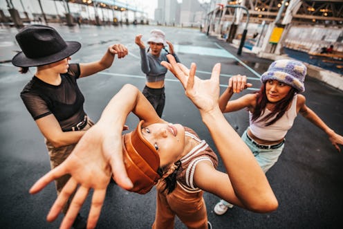 Group of four urban style professional dancers dressed with street-style clothes performing in the c...