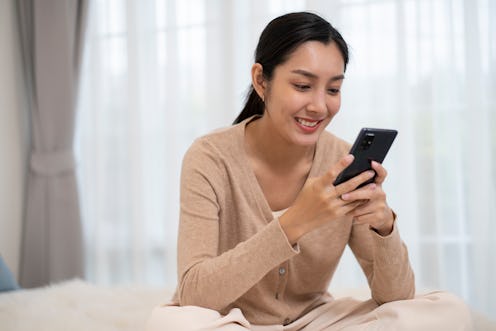 Close up of asian young woman lying on bed and holding mobile phone in her hands