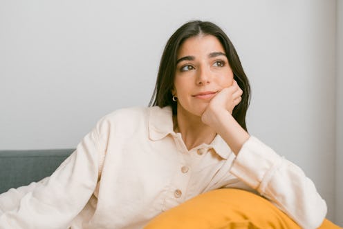 Relaxed young woman looking away while enjoying a pleasant time sitting on a sofa at home. Pensive a...