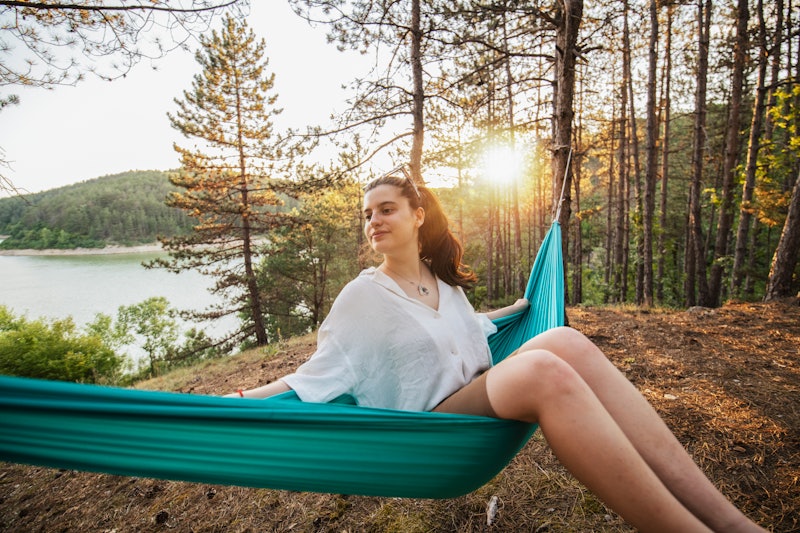 Young woman on camping in nature swinging and relaxing in hammock.