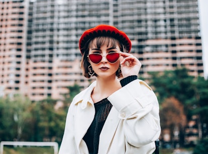 Beautiful girl in autumn clothes looks into camera. Young woman in red beret and red glasses