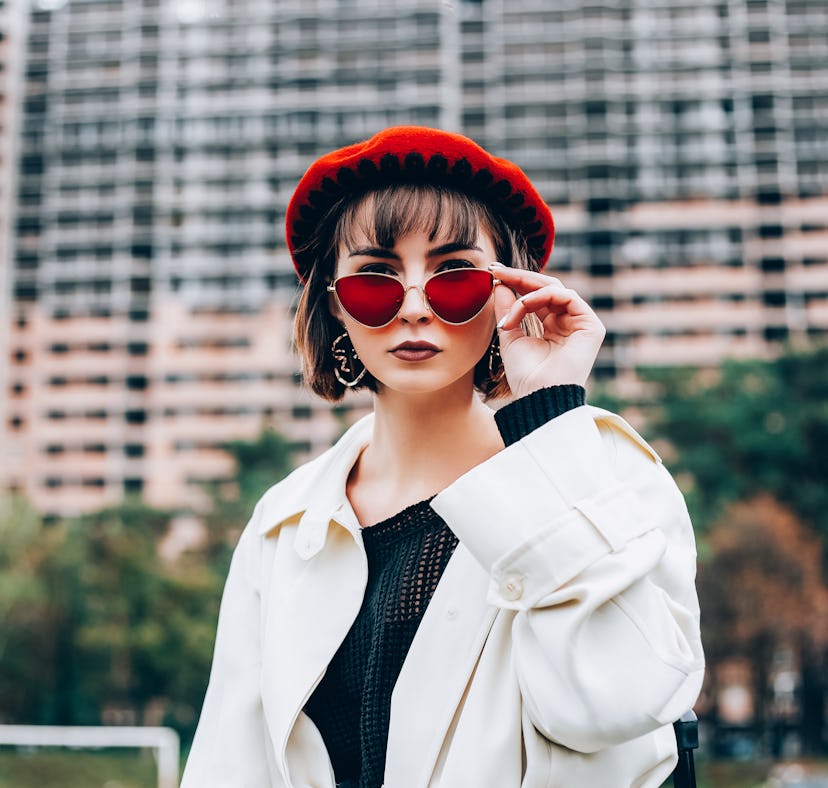 Beautiful girl in autumn clothes looks into camera. Young woman in red beret and red glasses