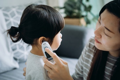 Young Asian mother checking daughter's temperature with a digital thermometer, as fever is a sign of...