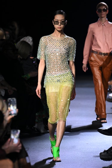 A model wearing Miu Miu's transparent yellow skirt and rhinestone t-shirt styled with neon green san...