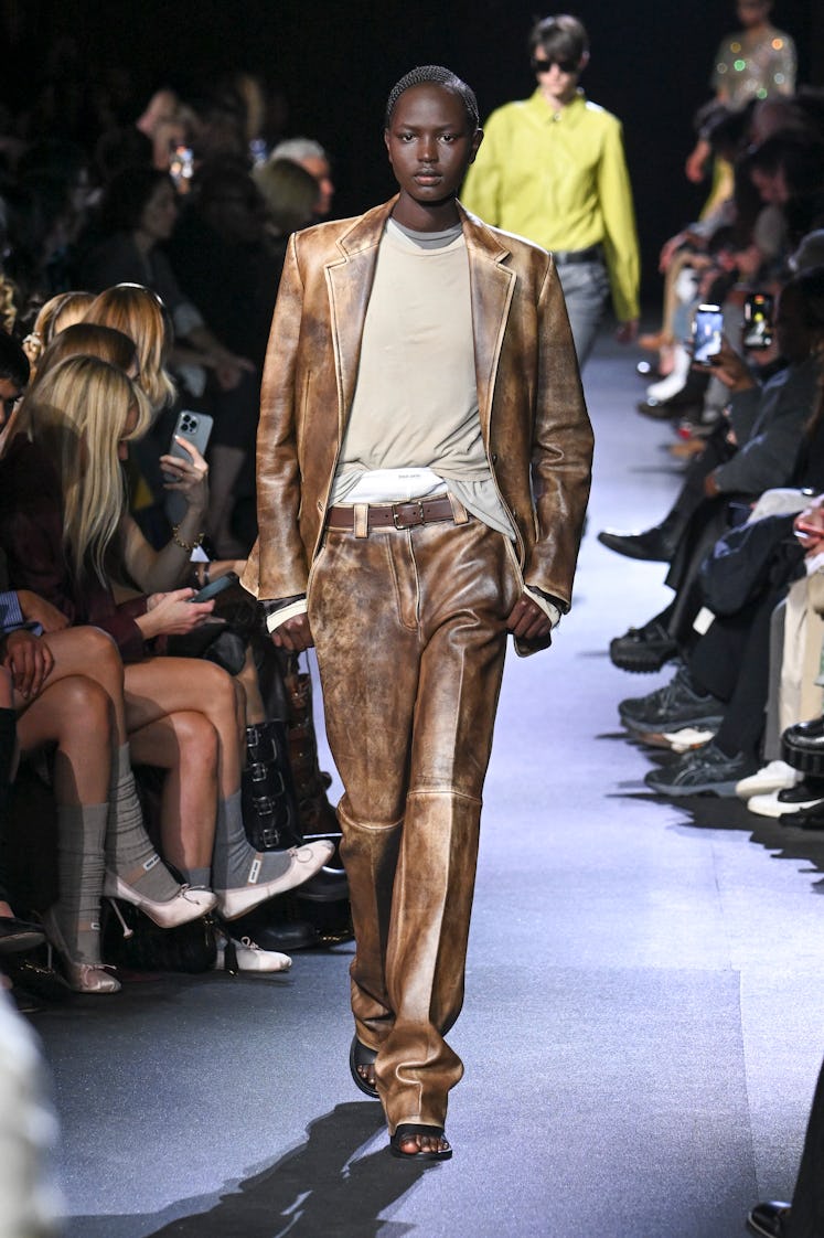 A model wearing a brown Miu Miu leather suit styled with nude cotton sweatshirt at Paris Fashion Wee...