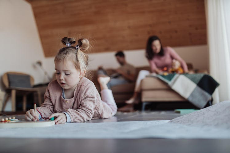 Little kid playing on the floor in living room, her parents in background sitting on a sofa.