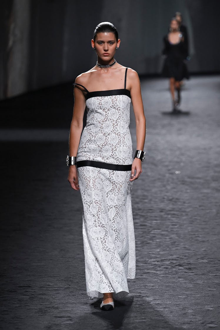 A model wearing a Chanel maxi black and white lace dress with ballerina shoes and oversize bracelets...