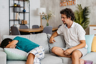 Young father sitting on the sofa in the living room and scolding his crying son.